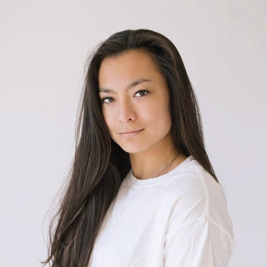 a woman with dark hair wearing a white tshirt looking into the camera with a white background behind her